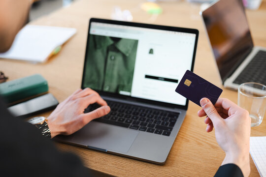 A person uses a credit card to make an online purchase on a laptop, demonstrating modern e-commerce and digital transactions.