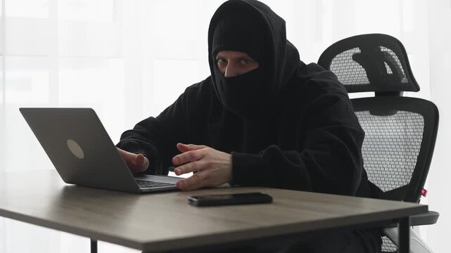 A scammer in a black balaclava with a laptop.
Hacking a laptop password.
Financial fraud.
Hacker in a black mask.