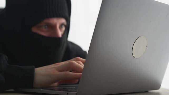 An anonymous hacker with a laptop.
A hacker in a balaclava sits at a laptop.
A masked hacker hacks a server.