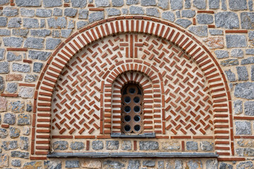 Obraz premium An architectural window, featuring a semicircular arch and small circular panes, set within decorative brick and stone masonry patterns at Church of Saints Clement of Ohrid and Panteleimon.