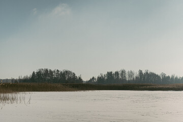 winter landscape with a lake covered in snow and a dark forest in the background