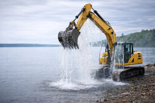 The excavator draws water with a bucket near the rocky shore. Space for text.