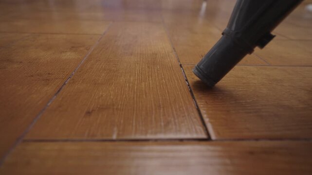 Close-up of vacuum cleaner nozzle moving across wooden parquet floor, effectively cleaning surface and grooves, highlighting routine housework and home hygiene, closeup, slow motion.