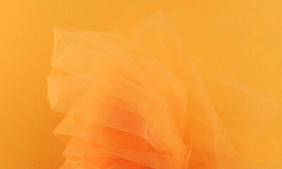 Bright orange yellow tulle fabric on yellow background.  Abstract transparent material curve wave.