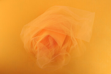 Bright orange yellow tulle fabric on yellow background.  Abstract transparent material curve wave.