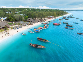 Aerial view of tourist boats and traditional fishing boats anchored in sea along the white sand beach of Zanzibar island. Turquoise Indian Ocean. tropical resort with bungalows in summer. Top view © den-belitsky