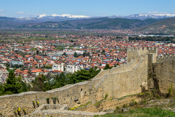 Obraz premium Panoramic perspective of Ohrid city, with red-roofed houses sprawling below the ancient walls of Samuel's Fortress, framed by distant snow-capped mountains.