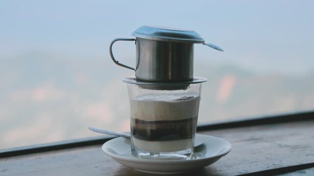 A Vietnamese coffee maker sits atop a glass of layered coffee in Yen Minh, Ha Giang, Vietnam. The traditional method brews a strong, rich cup, a cultural experience.