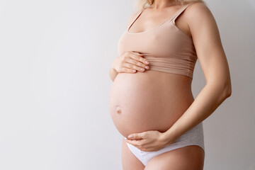 Closeup of impersonal woman, future mother touching naked tummy belly at third trimester showing love, care to baby standing at wall. Pregnant, eco, prenatal maternity concept. Isolated, copy space