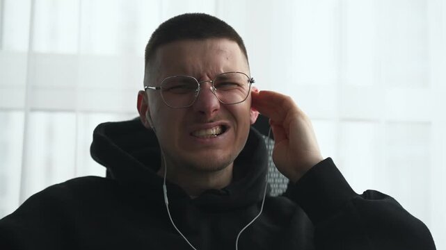 A man removes headphones from his ears due to severe pain.
Listening to loud music on headphones