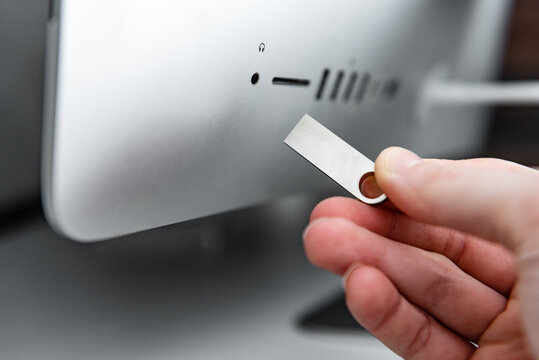 Hand holding silver USB flash drive connected to on the back of the monoblock.