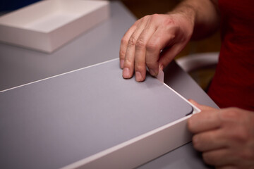 Minimalist studio shot of removing slim gray tablet from packaging. Product viewing scene showing hands unboxing modern sleek gray tablet from protective foam container