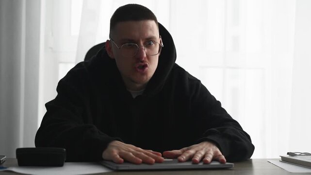 An angry office worker at his computer desk.
The man is yelling and angry.
The guy in the black sweater is angry.