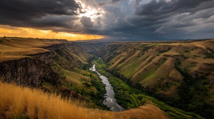 Fototapeta premium Breathtaking Aerial View of Canyon Landscape Under Dramatic Sky with Golden Sunset, Lush Green River and Rugged Hills in Nature’s Serenity