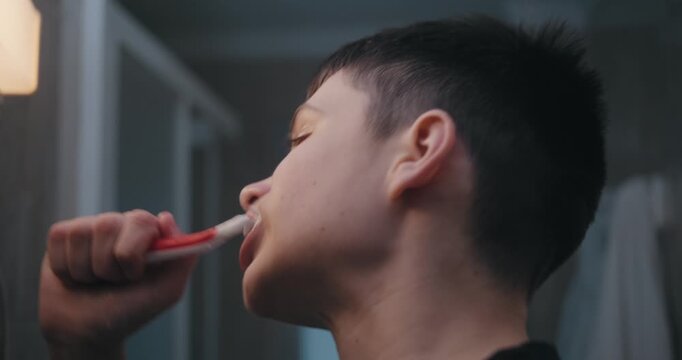 Teenage boy brushing his teeth in front of a mirror in the bathroom.