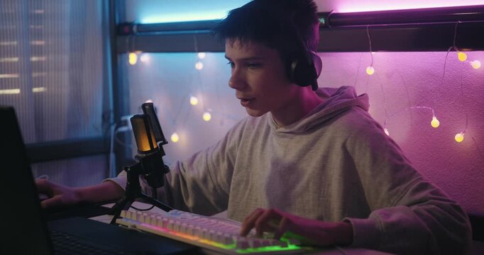 Teenage Boy Gamer in Headphones Playing an Online Computer Game at Night