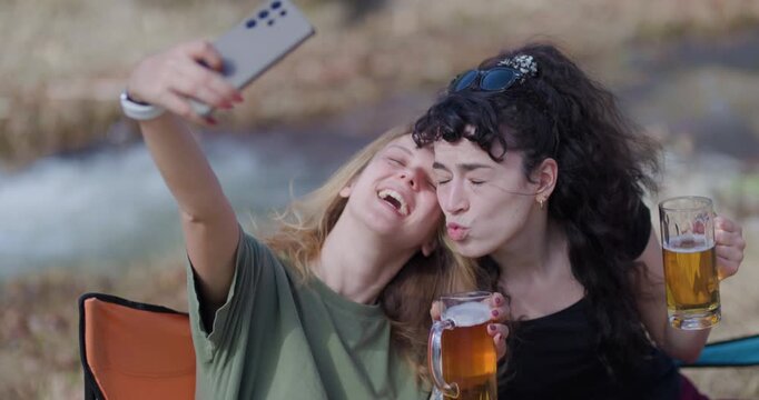 Two Female Friends Enjoying Drinks, Taking Selfies, and Making Memories at a Campsite by the River