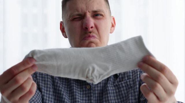A smelly white sock.
A man inhales the smell of a smelly sock.
Dirty white socks in a guy's hands.