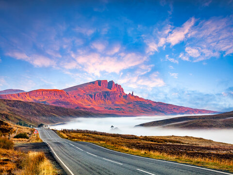 The Storr, Isle of Skye, Scotland, on a sunny autumn morning, as the sun rises and light hits the ridge. Loch Fada is beside the road, shrouded in mist.