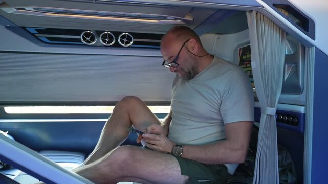 Sleeper Bus Relaxing Photo Browsing. Individual Resting Comfortably While Viewing Pictures On Phone Indoors. Person Leisurely Peruses Photographs Amid Cozy Cabin Environment With Soft