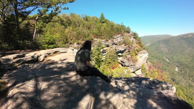 Woman Overlooking Landscape. Female Traveler Gazing At Mountains. Lady Seated On Edge Viewing Vast Valley. Woman Resting On Ledge Observing Expansive Mountain And Sky Scene