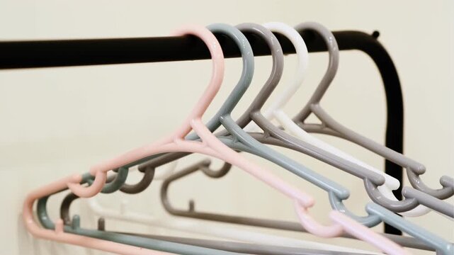 A close-up shot of a row of colorful plastic coat hangers (pink, blue, white, and purple) hanging on a black metal rack. Clean, minimalist background, perfect for lifestyle or retail imagery.