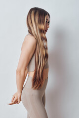 Young woman with long braided hair wearing beige outfit standing sideways against white background. Profile portrait with natural light and casual style. © SHOTPRIME STUDIO