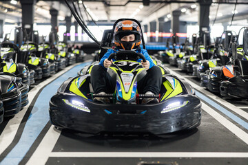 A young driver confidently holds the steering wheel in a decorated go-kart at a racing venue. © Dejan