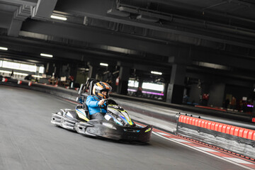A young racer driving swiftly on an indoor go-kart track, showcasing excitement and speed.