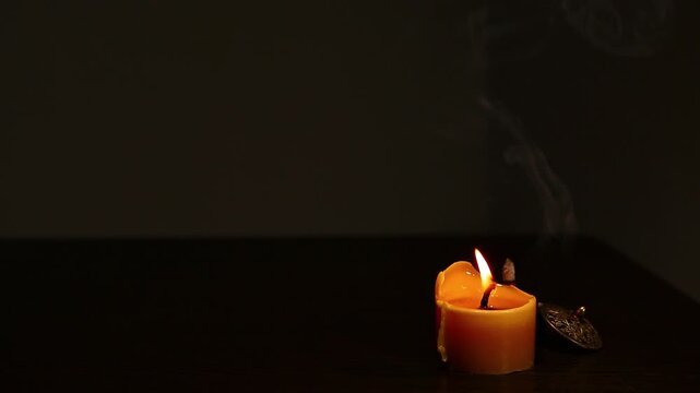 Burning candle fire near a smoldering aroma incense in incense holder on black background with copy space. Yoga therapy, spa fumigation, mental health, deep clear breath Closeup objects