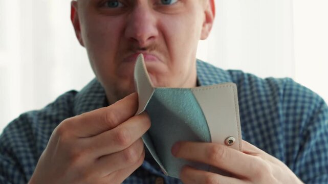 A man opens his empty wallet and gets angry that he has no money.
A wallet without money