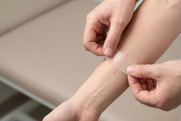 A person applies a clear silicone scar treatment patch to a small scar on their forearm.