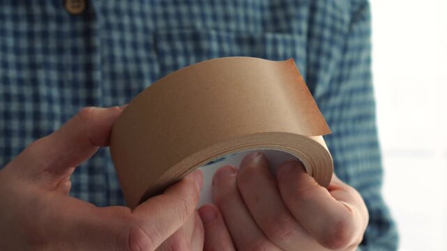 A man in a blue shirt unrolls adhesive tape from a roll.
A roll of adhesive tape in the hands of a technician.
Brown tape.