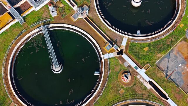 Top down view of wastewater clarifier with green water. Circular sedimentation tank filled with green water and a rotating bridge.