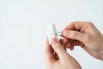 A person is using a SIM card ejector tool to open the tray on a white mobile device or router.