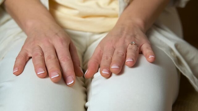 Nervous woman's hands fidgeting with engagement ring. Close-up of a woman's manicured hands resting on her knees, nervously fidgeting and showing her anxiety through restless finger movements