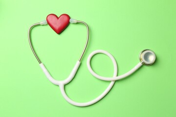 Fototapeta premium Measuring blood pressure. Stethoscope and heart figure on light green background, top view