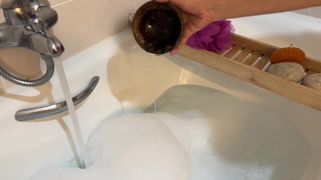 Mano vertiendo aceite de ba&ntilde;o en el agua desde un cuenco