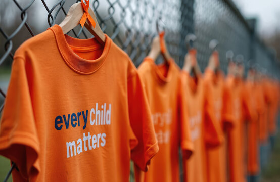 Orange shirts with every child matters text hang on fence. Silent protest shows solidarity for missing and murdered indigenous children. Remembering residential school survivors and their families.