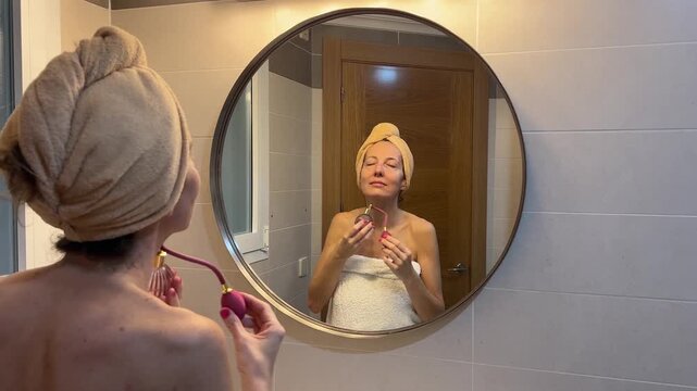 Mujer aplic&aacute;ndose perfume frente al espejo en su rutina de cuidado