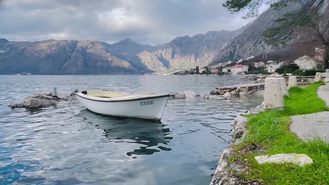 Boat grass quay bay mountains reflection calm. White dinghy tied near green bank, gentle waterline and mossy stone edge, distant