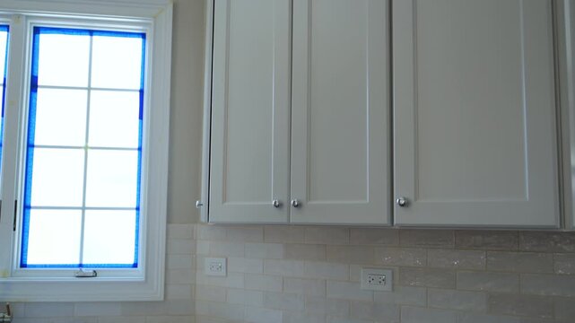 Close-up of newly installed white kitchen cabinets near window, professional kitchen cabinet installation and modern home renovation concept.