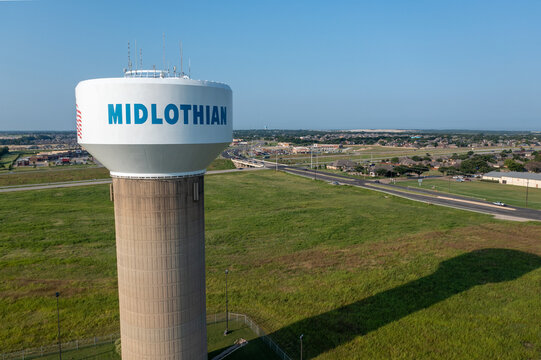 Aerial Drone View of Tall White Water Tower in Green Grass Lawn With Buildings in the Distance in Midlothian, Texas