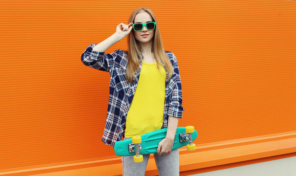 Stylish young woman with skateboard, modern teenage girl posing on city street