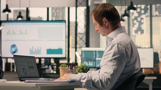 Man worker analyzing KPI metrics and performance review data in corporate office workspace. Visual data, charts and analytics dashboard supporting objectives, planning and development.