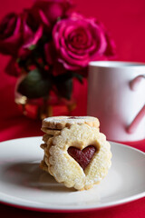 Close-up of a homemade heart-shaped cookie filled with fruit jam and lightly dusted with powdered sugar, served on a plate in a cozy kitchen setting. This image captures the warmth of home baking and 