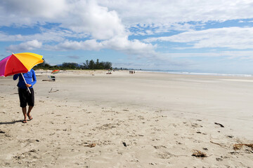 Obraz premium an unrecognizable young man walking on the beach with a colorful parasol.