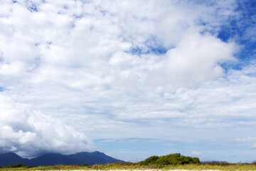 Landscape showing a small patch of land with green grass at the bottom of the photo, mountains in the background on the left, and a cloudy sky that dominates most of the image