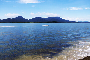 Beautiful landscape where small boats cross the calm, clear sea on a bright day with diffused light, mountains in the background and a blue sky with clouds