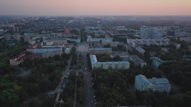 Aerial evening view of Orel city in Russia with river, Strelka, main buildings, churches and roads. Beautiful cityscape with lights reflecting on water at sunset, showing urban architecture, skyline.